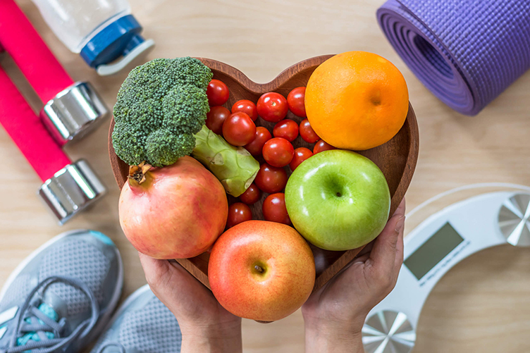 A man holding a bowl of fruit with a background of exercise equipment