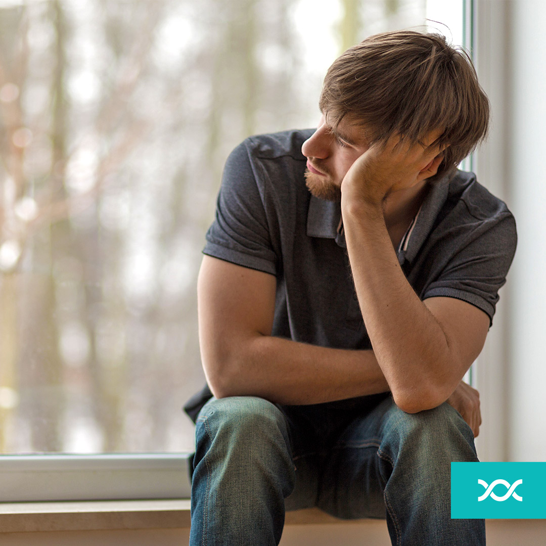 Thoughtful young man sitting on a windowsill looking in the distance